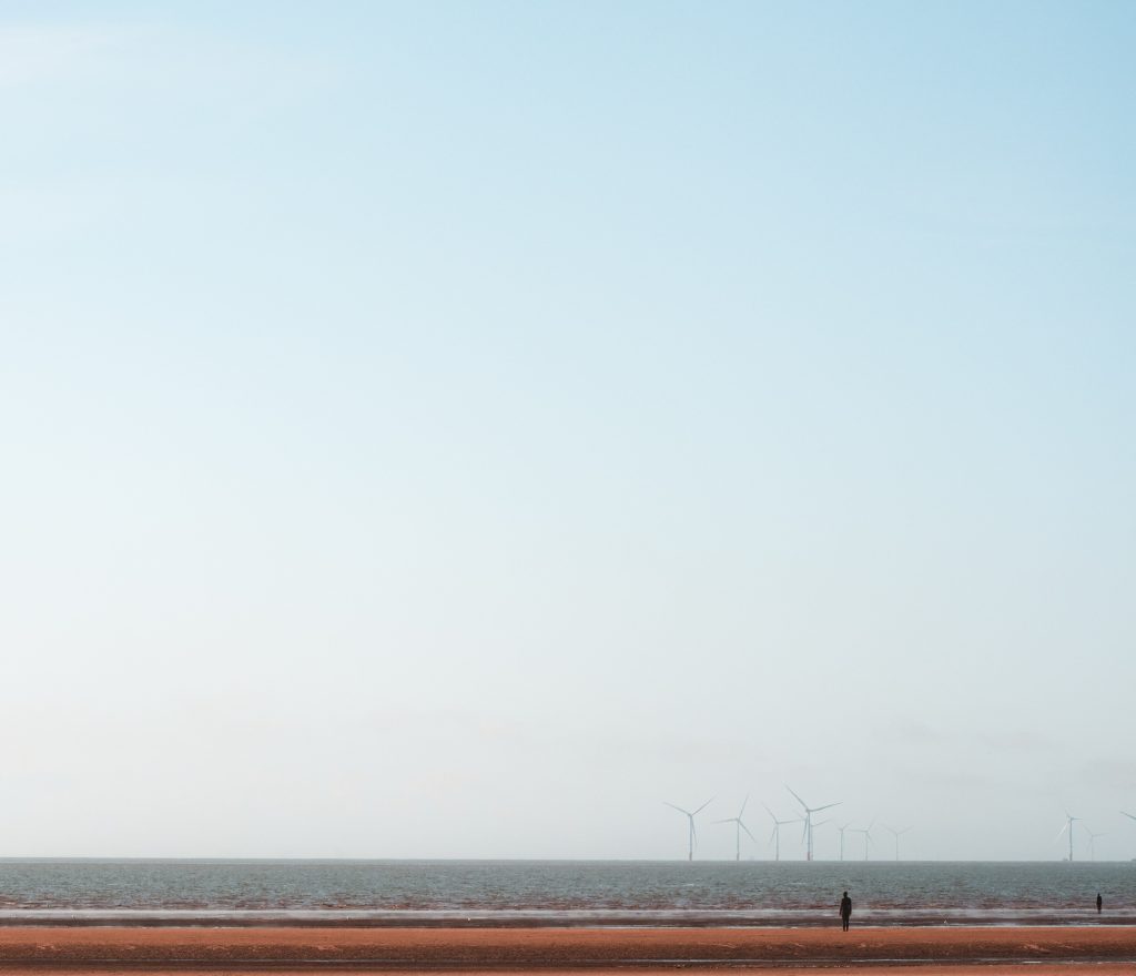 une plage avec un champt d'éoliennes au loin